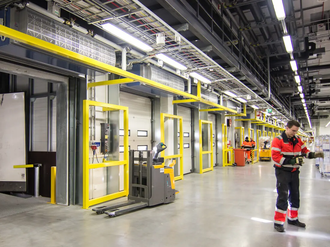 Ilmaverhot logistiikkakeskuksen lastausovien yläpuolella, etualalla työntekijä ja haarukkavaunu